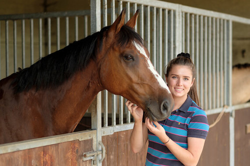 Girl smiling by horse who is stood at their stable door