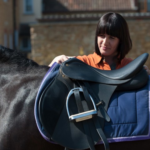 rider putting saddle on horse