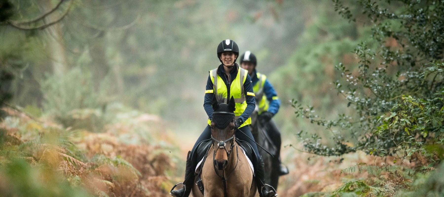 two riders on a horse in nature wearing hi vis