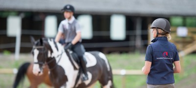 Coach in complete horsemanship with a horse and rider on the background