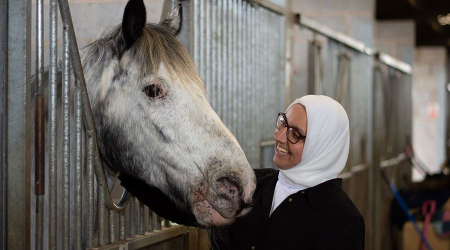 woman smiling at a horse in stables