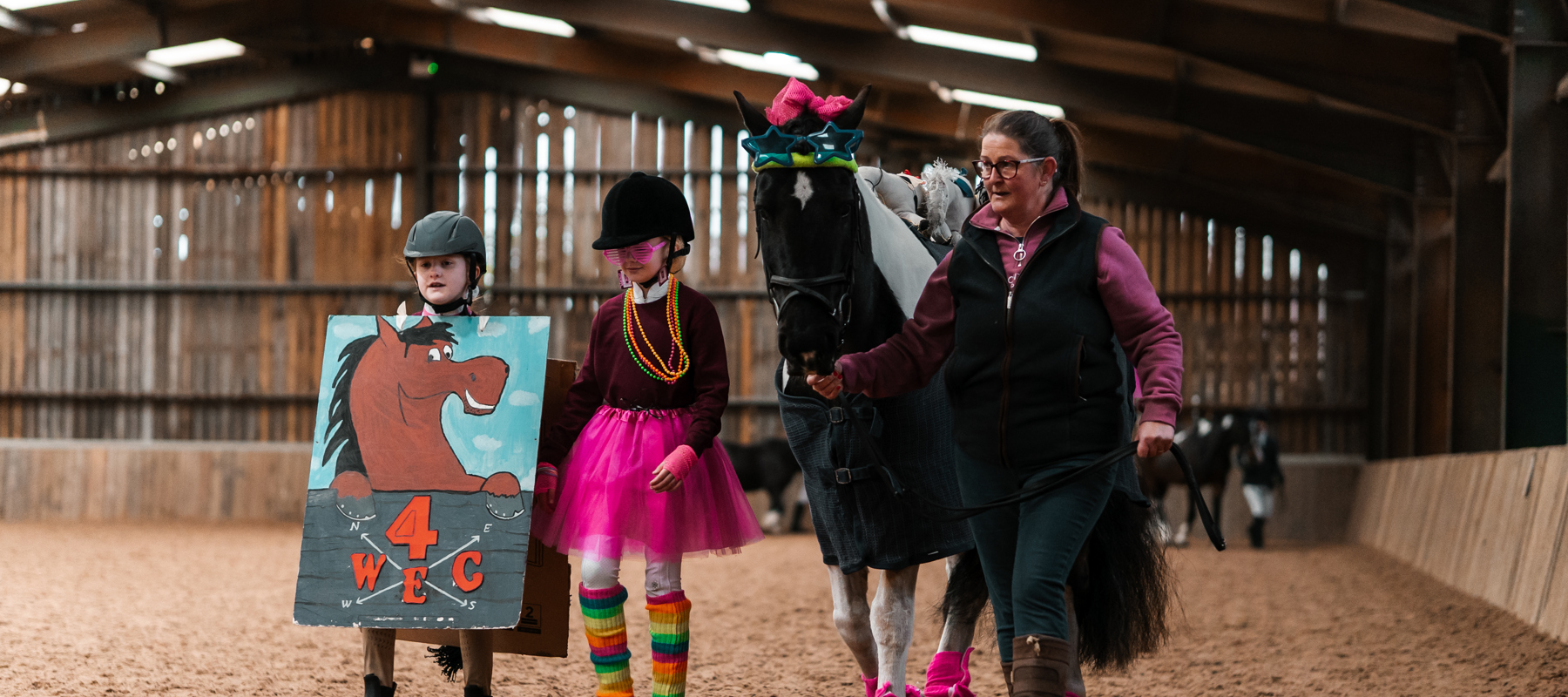 Two children in fancy dress walking alongside a horse being led by an adult in an inside arena